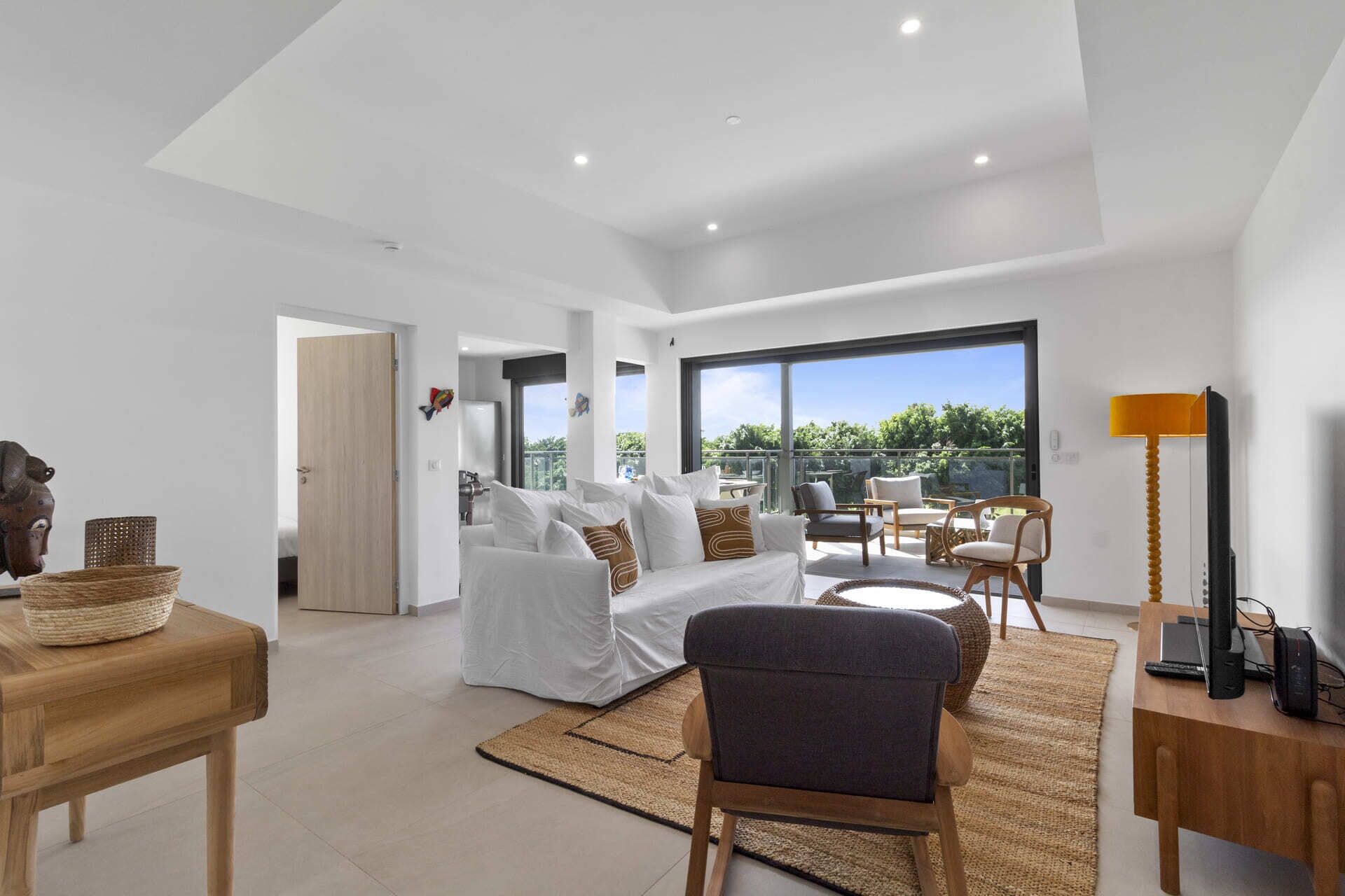 A spacious living room with a large window, a sofa set, a wooden coffee table, and a modern lamp.