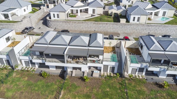 A modern residential complex with multiple houses featuring sloped roofs, a swimming pool, and a stone retaining wall.