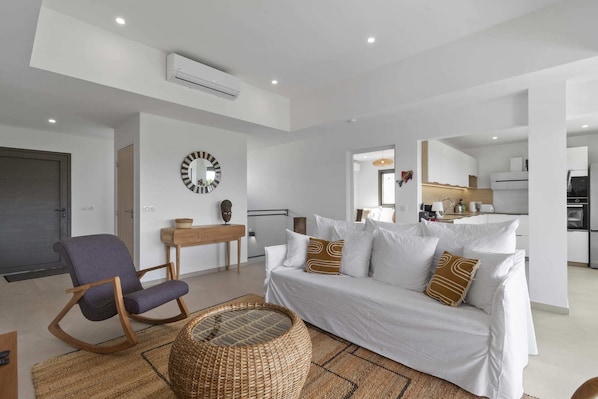 A modern living room with a white sofa, a wooden side table, and a wicker coffee table.