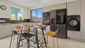 A modern kitchen with a dining area, a washing machine, and a clock on the wall. - Villa Arlet - Three Bedroom Villa, Sleeps 6 (Les Anses-d'Arlet)