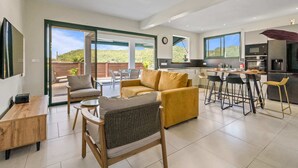 A spacious living area with a sofa, chairs, a dining table, and a kitchen area with a bar. - Villa Arlet - Three Bedroom Villa, Sleeps 6 (Les Anses-d'Arlet)