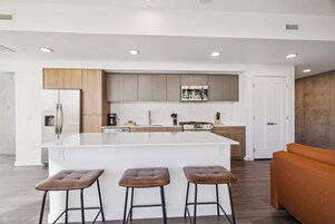 A modern kitchen with a central island, three stools, and a wooden bench.
