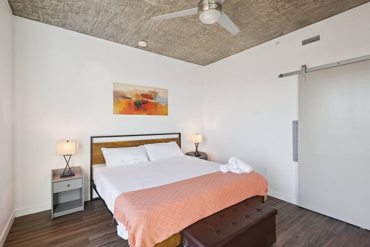 Una habitación de hotel moderna con una cama, mesitas de noche, un ventilador de techo y un cuadro en la pared.