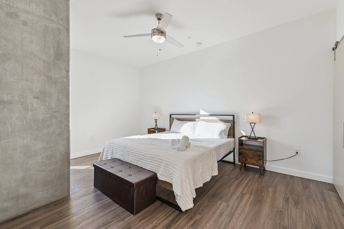 Un dormitorio con cama, banca, ventilador de techo y lámparas de noche.