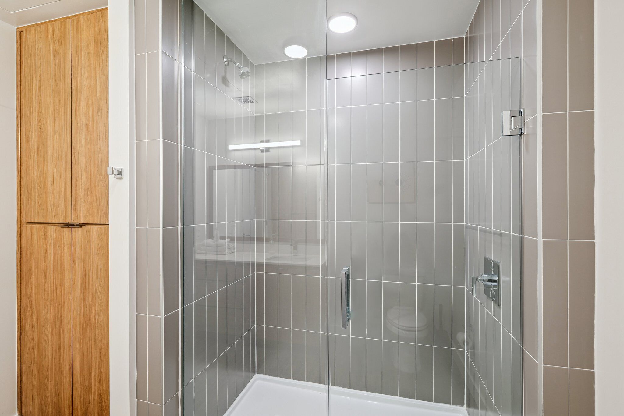 A modern bathroom with a glass-enclosed shower, a wooden wardrobe, and a white bathtub.