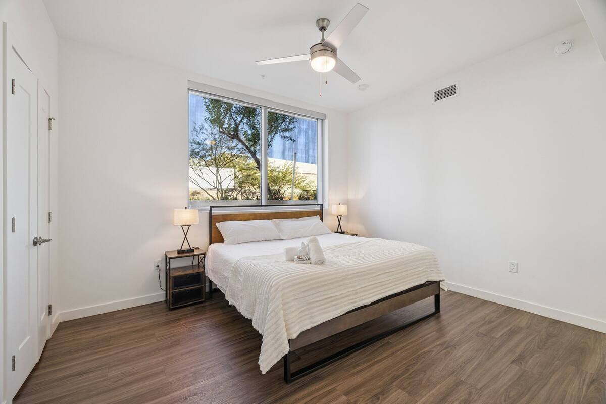 Un dormitorio con cama, ventilador de techo, ventana y mesita de noche con lámpara.