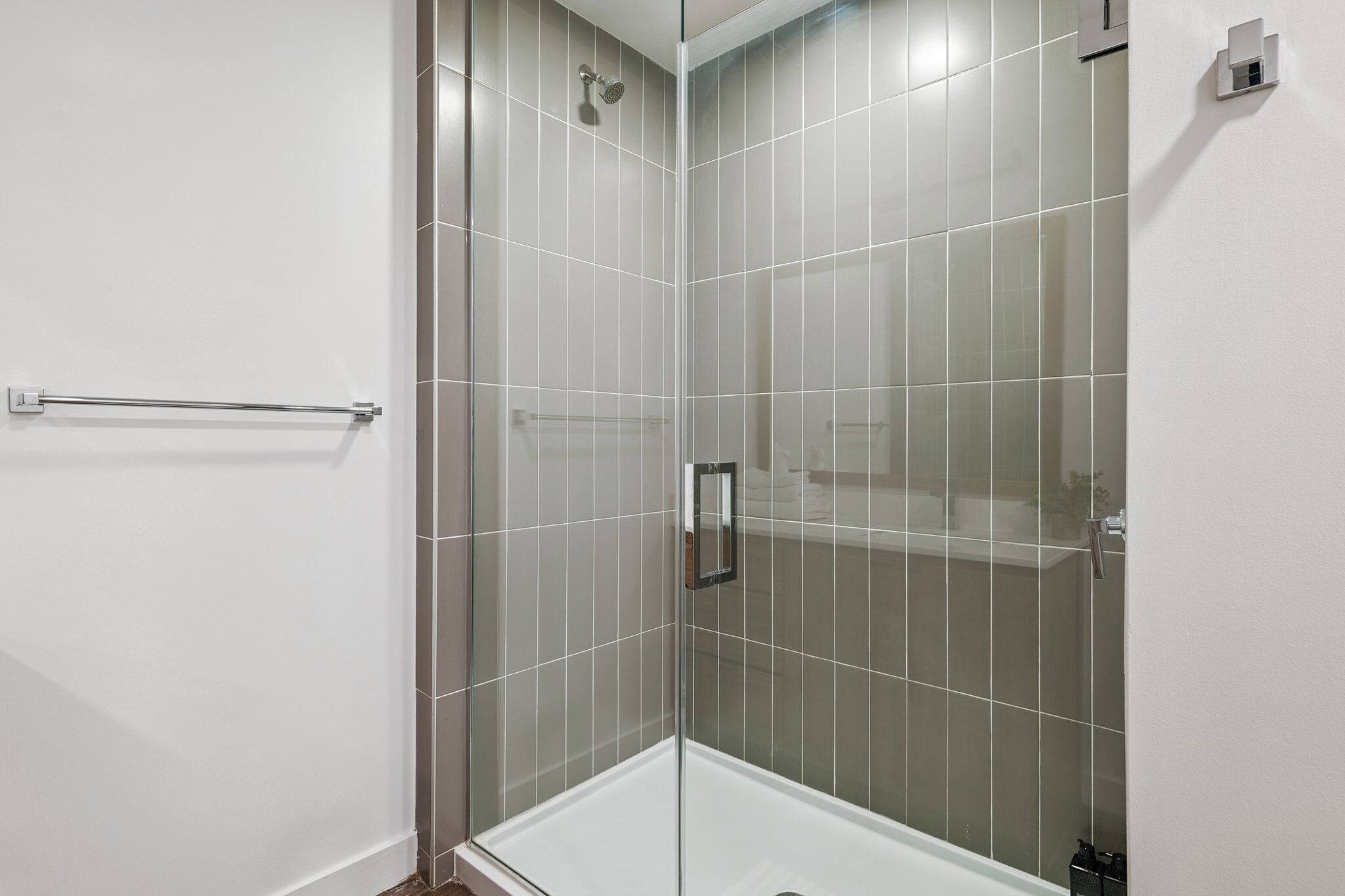 A modern shower with clear glass doors, a handheld showerhead, and a towel rack.