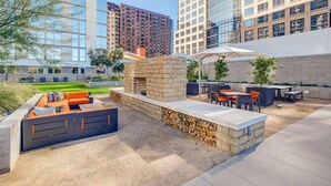 An outdoor patio area with seating, a stone fireplace, and a view of surrounding high-rise buildings. - CozySuites at ADELINE (Phoenix)
