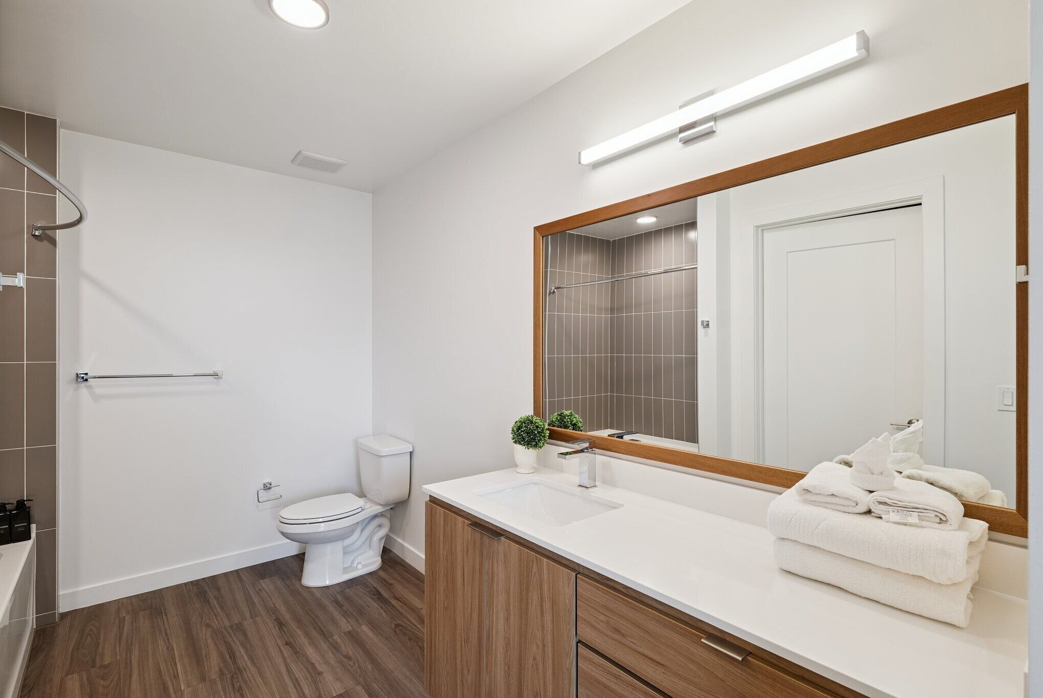 Une salle de bain moderne avec des toilettes blanches, un lavabo avec un miroir et un espace douche.