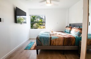 Quarto com cama, televisão, janela e ventoinha no teto.