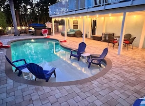 A swimming pool with lounge chairs and a table, surrounded by a covered patio area with seating and a basketball hoop. - Ultimate Beach Getaway (Fort Myers Beach)