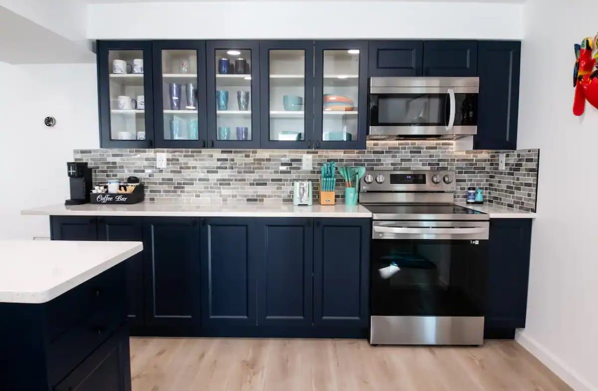 Une cuisine moderne avec des meubles de couleur sombre, un four à micro-ondes, un four traditionnel et une machine à café.