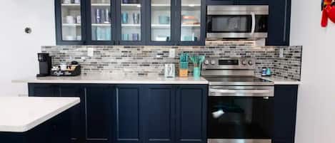 A modern kitchen with dark cabinets, a microwave, an oven, and a coffee machine.