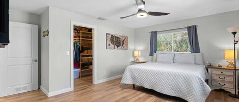 A bedroom with a bed, a ceiling fan, a window with curtains, a nightstand, and a closet.