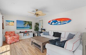 Ein Wohnzimmer mit einem weißen Sofa, einem roten, gemusterten Sessel, einem Holztisch und einem Deckenventilator.