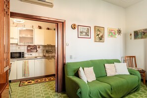 A room with a green sofa, a wooden chair, a kitchen with white cabinets, and a wall with framed pictures. - Peaceful House in the Heart of Tuscany, Near Florence and Siena (Vinci)