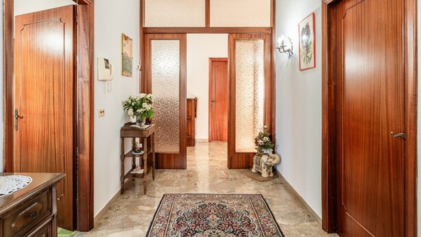 Un pasillo con puertas de madera, un tapete estampado y una pequeña estatua.