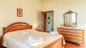 Una cama bien hecha con toallas dobladas, un aparador de madera con cajones, un espejo y un cuadro en la pared.