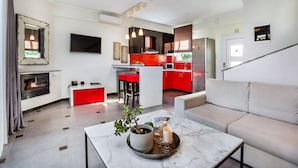 Uma sala de estar moderna com um sofá, uma mesa de centro com velas e uma área de cozinha com armários vermelhos e uma televisão.
