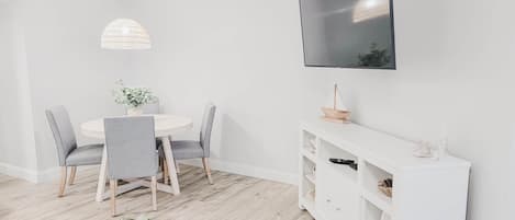 Un comedor con una mesa redonda, sillas grises, una lámpara colgante, una consola blanca y un televisor montado.