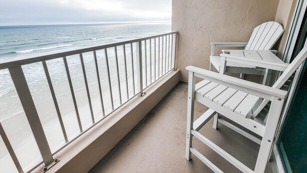 Un balcon avec vue sur l’océan, des chaises blanches et un mur de couleur beige.