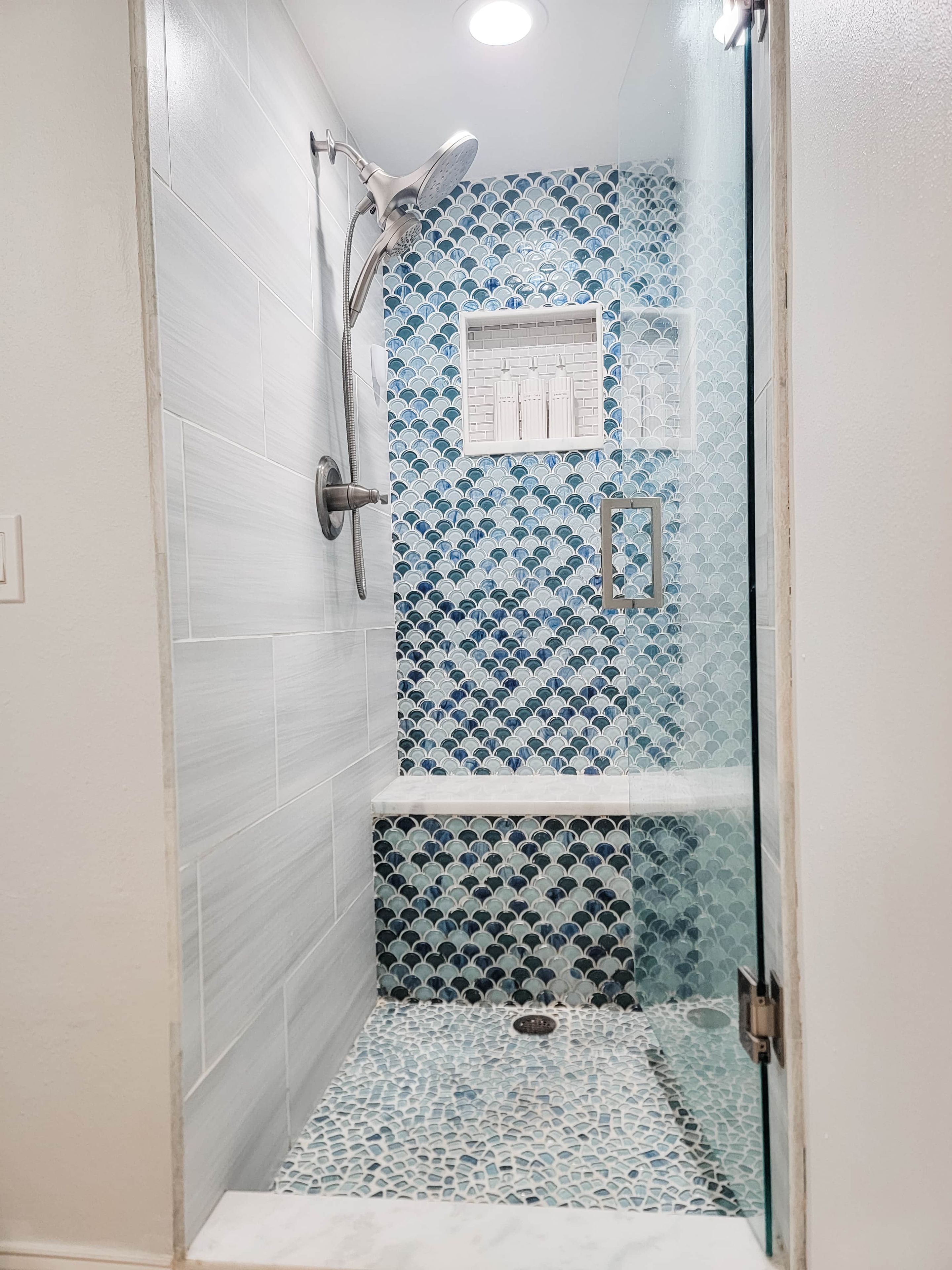 A shower with a glass door and a tiled wall with a blue pattern.