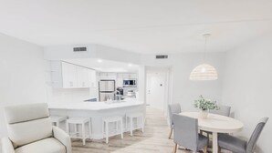 Une cuisine moderne avec des meubles blancs, un îlot central et un coin repas comprenant une table ronde et des chaises.