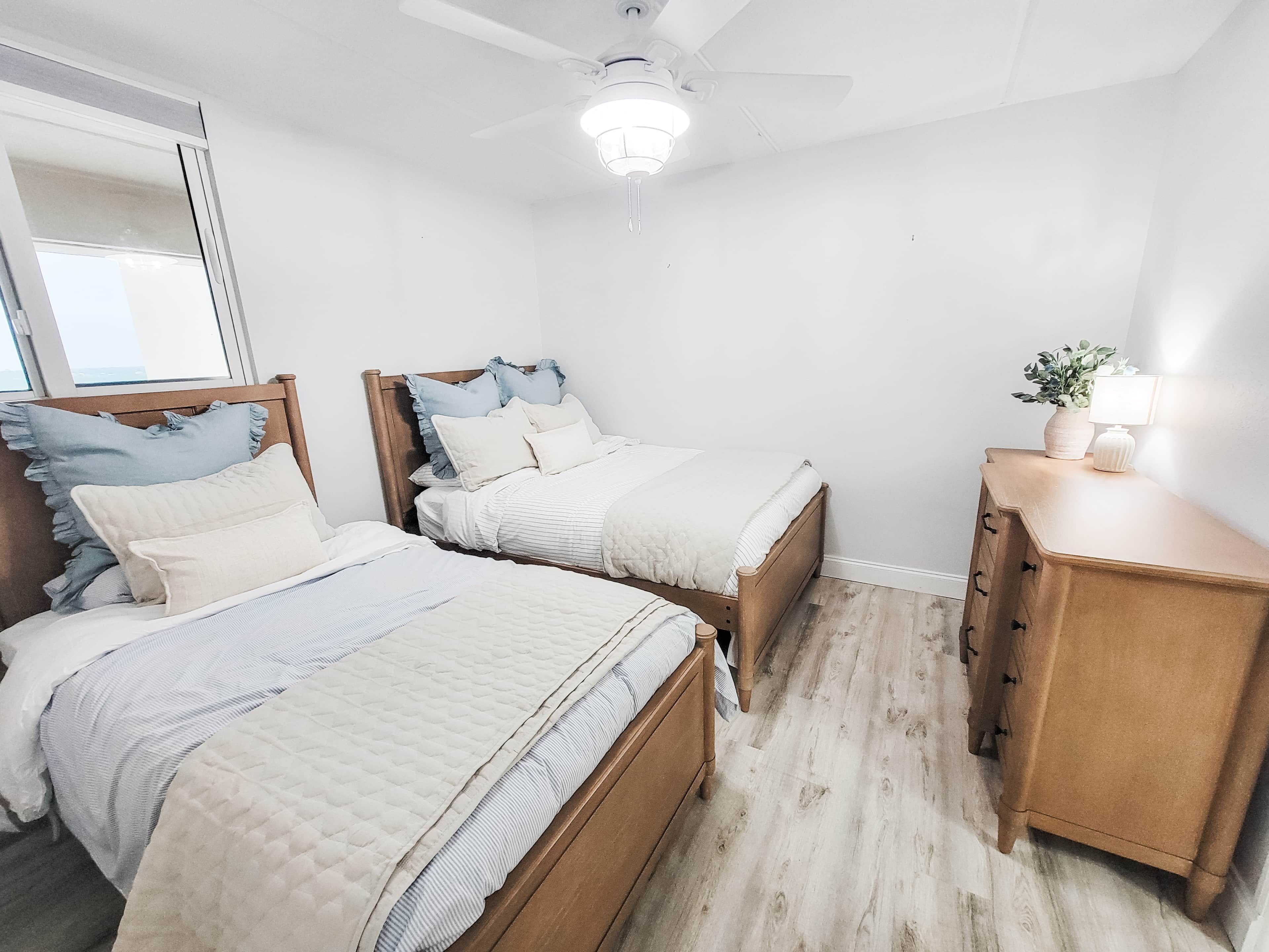 Une chambre avec deux lits, un ventilateur de plafond, une table de chevet et une commode.