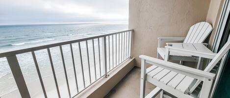A balcony with a view of the ocean, white chairs, and a beige wall.