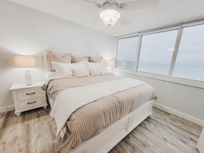 Ein Schlafzimmer mit Bett, Nachttischen, einem Deckenventilator und einem großen Fenster mit Blick.