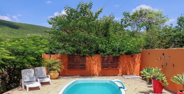 Une piscine entourée de chaises longues, elle-même bordée d’un jardin et d’une colline.