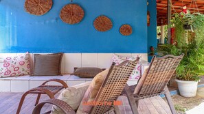 A blue wall with woven wall hangings, a white sofa with striped and floral cushions, wicker chairs, and a potted plant.