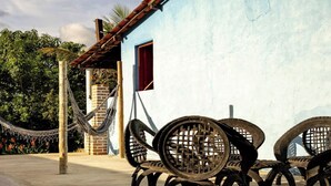 Un bâtiment à la façade bleue, avec un hamac et des chaises en métal.
