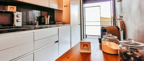 A modern kitchen with white cabinets, a wooden countertop, a coffee machine, and a view of the outside.