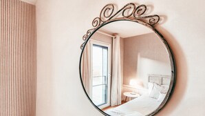A hotel room with a round mirror, a bed, a bedside table with a lamp, and a window with curtains. - Bridge view apartment in Sacavem (Sacavém)