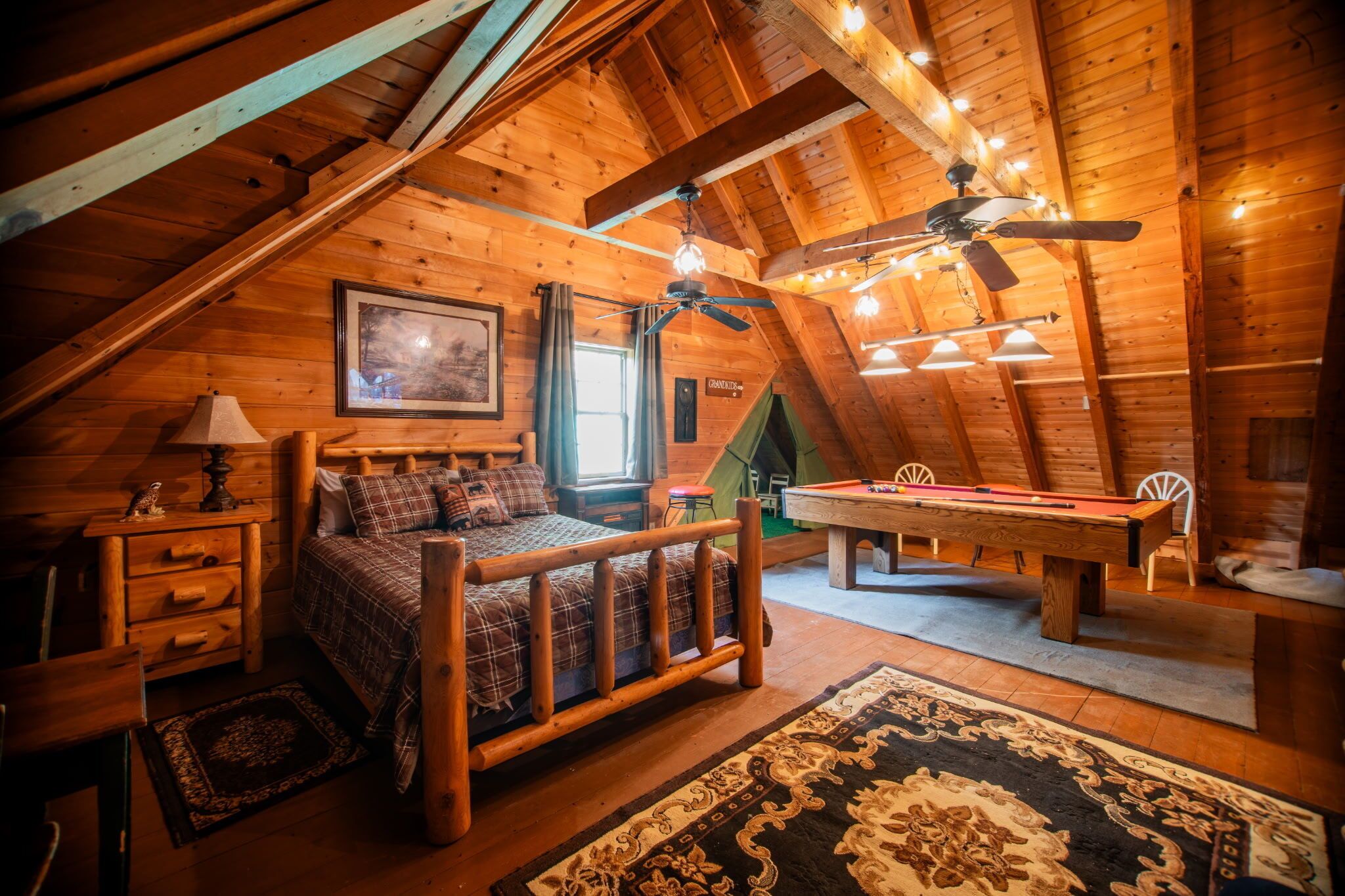 Ein gemütliches Schlafzimmer im Dachgeschoss mit Holzbalkendecke, einem Bett, einem Billardtisch und einem Deckenventilator.