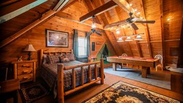 Ein gemütliches Schlafzimmer im Dachgeschoss mit Holzbalkendecke, einem Bett, einem Billardtisch und einem Deckenventilator.