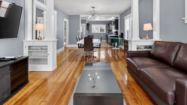 Una sala de estar moderna con un sofá de cuero marrón, una mesa de comedor con sillas, una zona de cocina y un televisor montado en la pared.