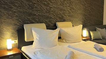 A neatly made bed with white linens and rolled towels, a dark textured headboard, and bedside lamps on wooden nightstands.