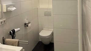 A modern bathroom with white tiles, a skylight, a toilet, and a sink with a towel rack.