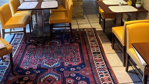 A dining area with stone walls, yellow chairs, a patterned rug, and framed artwork.