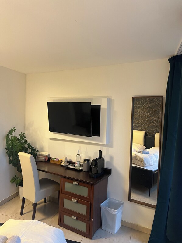 A hotel room with a bed, a desk with a flat-screen TV, a coffee maker, a trash bin, and a mirror reflecting the bed. - Hotel Scheunenwerk (Heroldsberg)