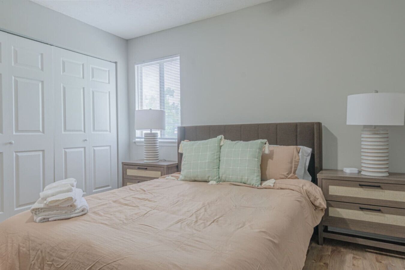 Un dormitorio con cama, mesitas de noche, ventana y puerta.