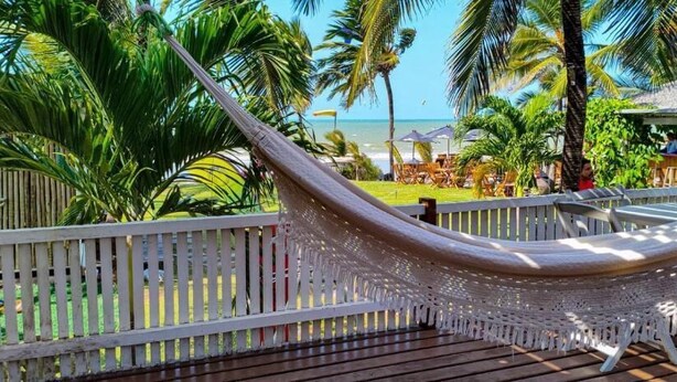 Een hangmat op een houten terras met uitzicht op het strand en palmbomen.