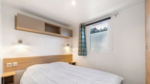 Ein Schlafzimmer mit einem Bett, Nachttischen, einem Wandregal, einem Fenster mit Vorhängen und einer Steckdose.