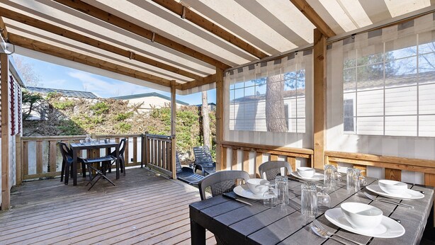 Ein überdachter Essbereich im Freien mit Tischen und Stühlen, einer Holzterrasse und Blick auf die umliegende Landschaft.