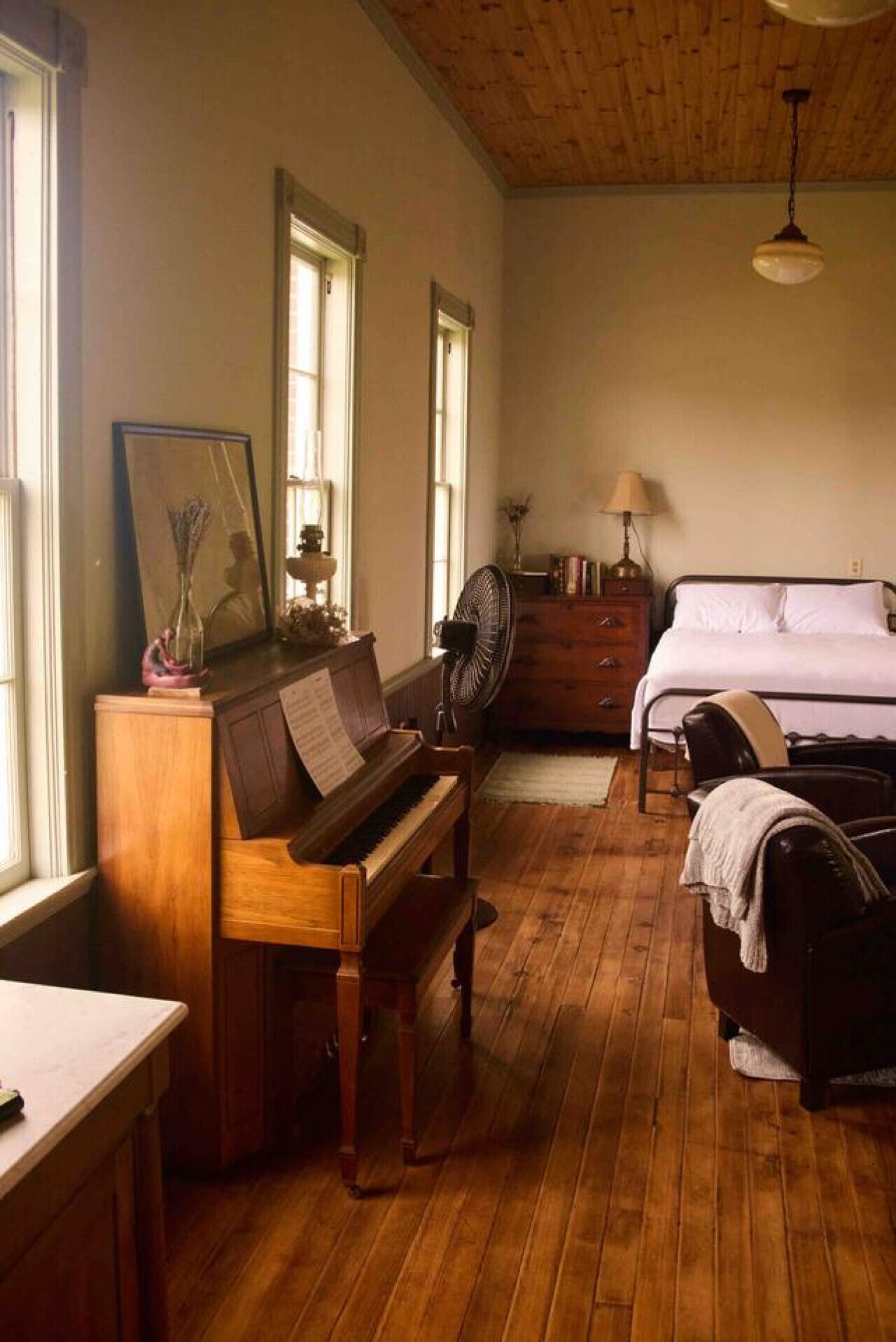 Una habitación con suelo de madera, un piano, una cama y un ventilador.