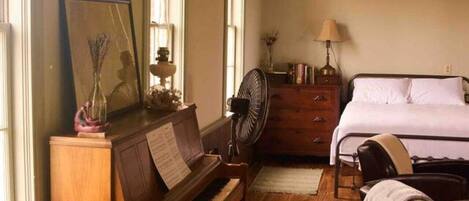 Una habitación con suelo de madera, un piano, una cama y un ventilador.