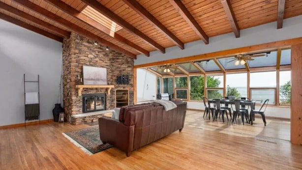 A spacious living room with a stone fireplace, wooden flooring, and a large window overlooking a scenic view.