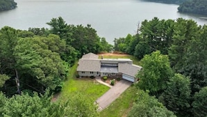 A two-story house with a garage, surrounded by dense trees and a large body of water in the background.